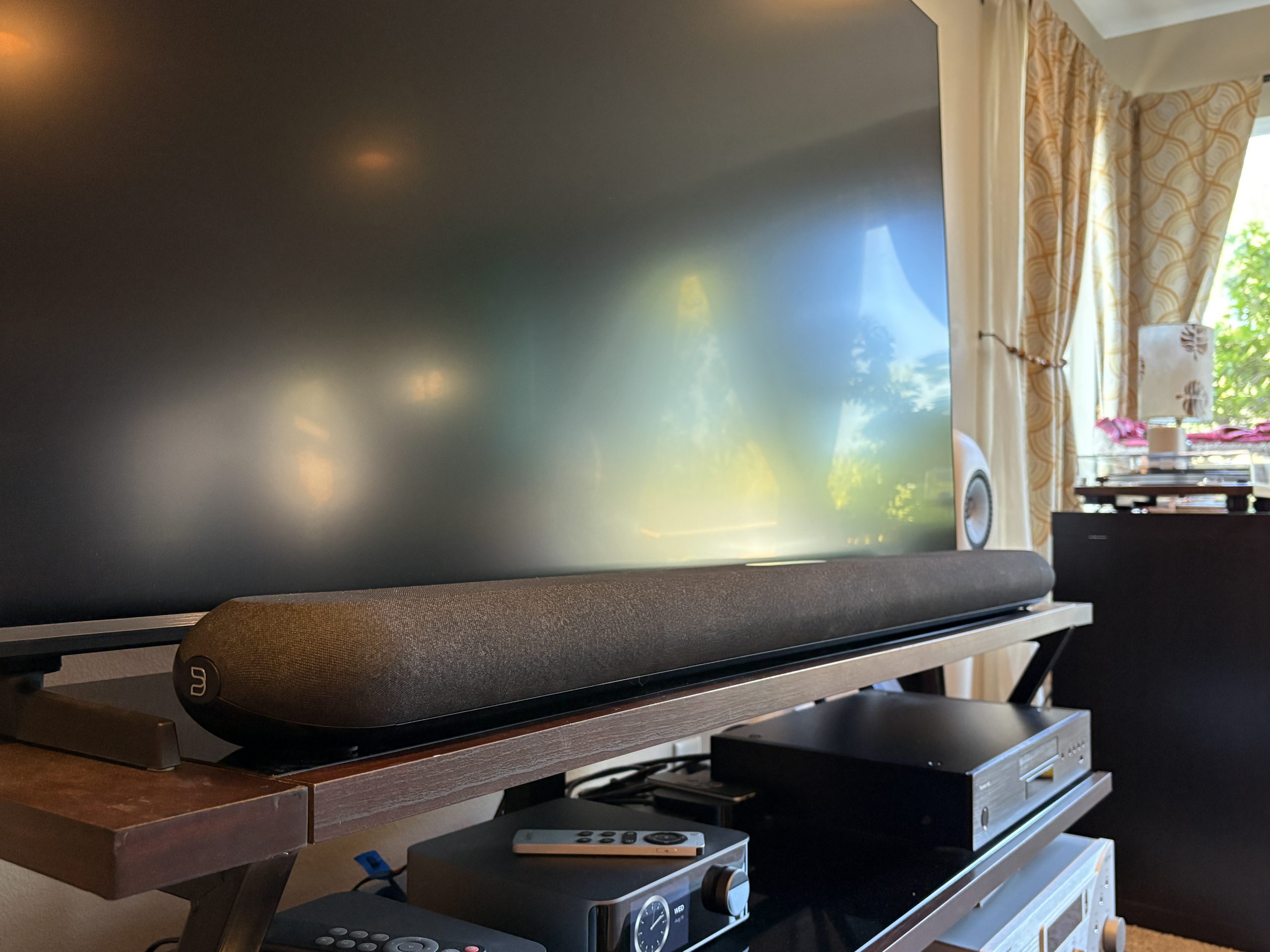 The Bluesound Pulse Cinema soundbar sits on a dark wood console in front of a black TV.