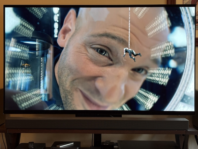 The Samsung QS90H soundbar sits on a brown console with a TV tuned to the film Ant-Man