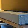 Samsung's HW-QS90H soundbar sits on a brown console below a black TV screen