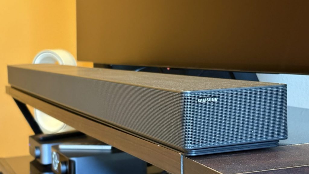 Samsung's HW-QS90H soundbar sits on a brown console below a black TV screen