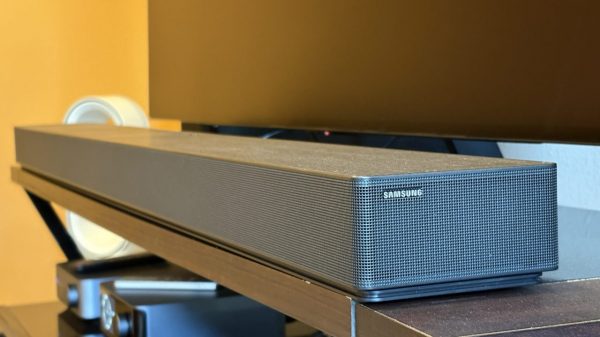 Samsung's HW-QS90H soundbar sits on a brown console below a black TV screen