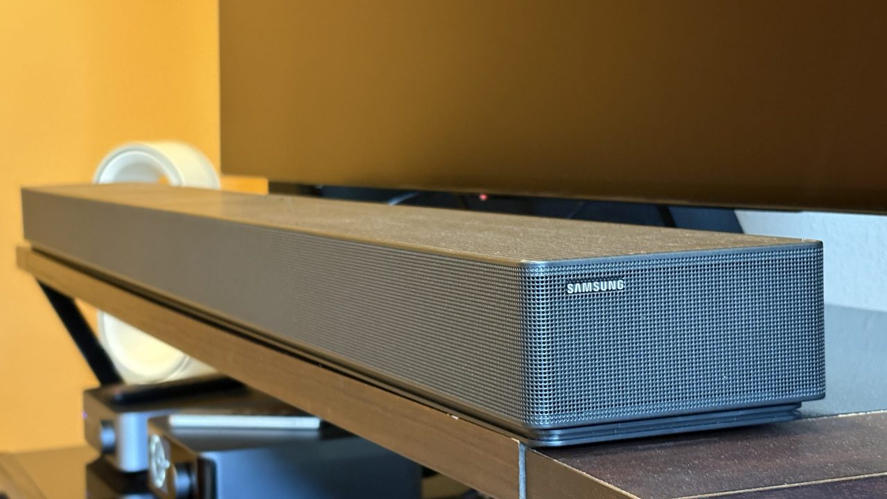 Samsung's HW-QS90H soundbar sits on a brown console below a black TV screen
