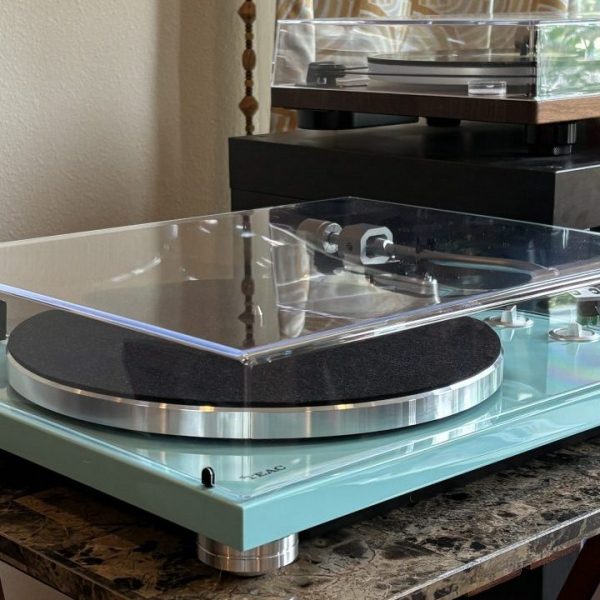 A turquoise TEAC TN-400BT-X turntable sits on a table next to a record console.